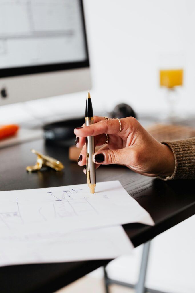 Preliminary Transfer Credit Review A woman's hand holding a pen, working on paperwork in a modern office setting.