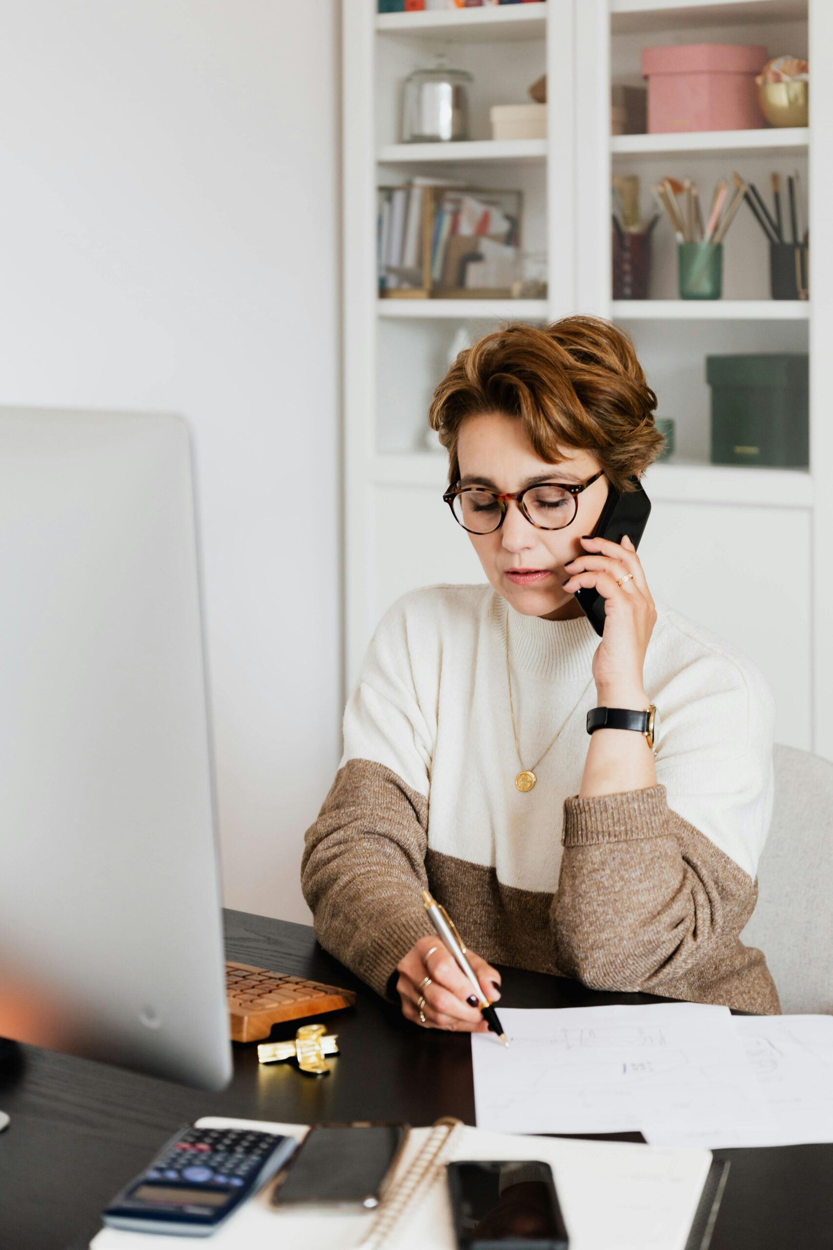 Preliminary Transfer Credit Review Professional woman multitasking in her workspace with phone and laptop.