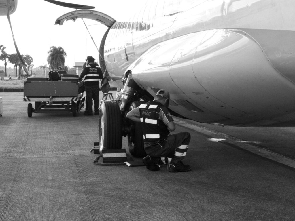 Black and white photo of a ground crew performing aircraft maintenance on the tarmac.