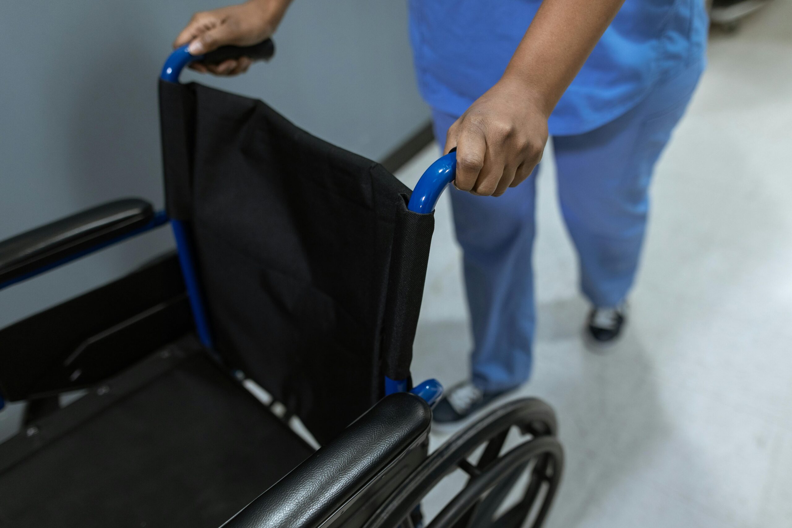 Close-up of a medical worker in scrubs pushing a wheelchair in a hospital setting.