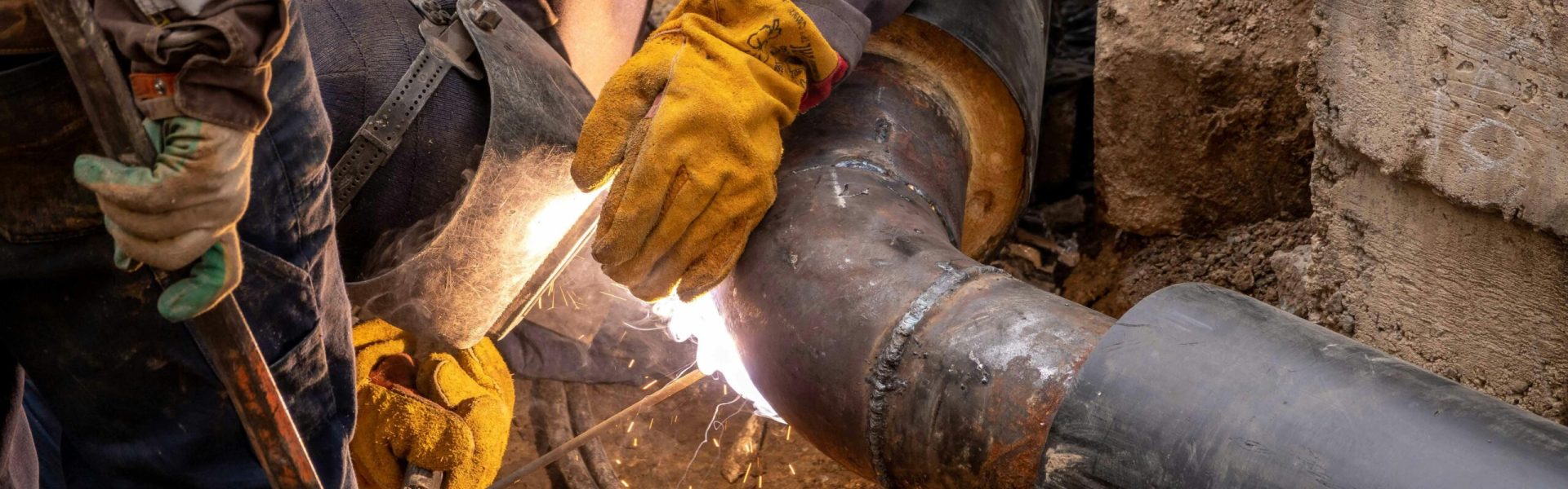 Close-up of a skilled worker welding steel pipes in an industrial setting, showcasing expertise and safety gear.